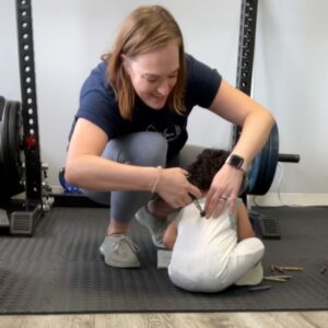 A picture of Dr. Olivia adjusting a young kid on the floor with an activator.